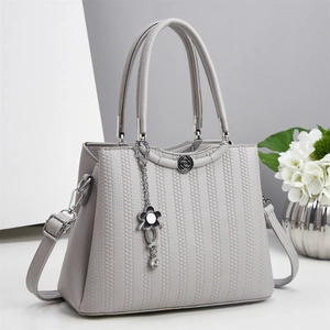 Bolso de mano gris claro con textura granulada, colgante floral y detalles plateados