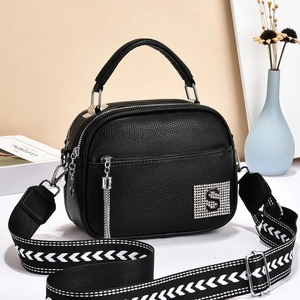 Minimalist black lychee pattern crossbody bag with wide strap and tassel in a clean room