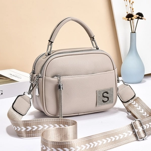 Detail of beige crossbody bag featuring textured lychee grain and tassel zipper design