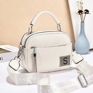 Detail of white lychee leather bag with wide strap, tassel zipper, and rhinestone S patch