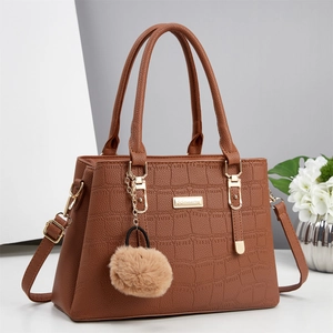 Detail of brown crocodile pattern handbag featuring a gold logo plate and plush ball charm
