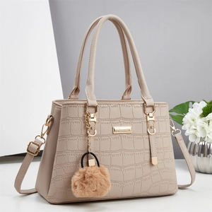 Detail of beige crocodile pattern handbag with gold hardware and plush pompom charm