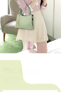 Détail du sac à main vert clair texturé avec breloque feuille dorée et double anses