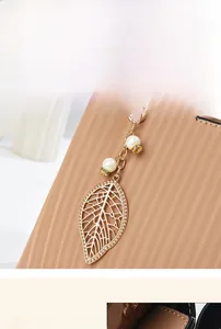 Détail de breloque feuille dorée avec perles et texture gaufrée sur un sac cabas beige