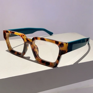 Detail of square glasses with tortoiseshell frame and contrasting teal temples on stand