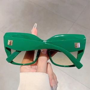 Gros plan détaillé de lunettes de soleil en résine vert foncé avec clous dorés et verres dégradés