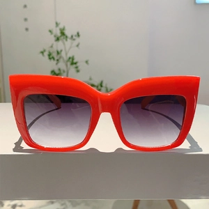 Détail de lunettes de soleil œil-de-chat rouges avec verres dégradés violets sur socle