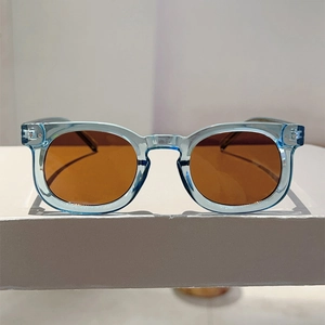 Detail of round light blue acetate sunglasses frame with brown lenses on white stand