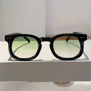 Close-up of retro black frame sunglasses with silver rivets and gradient green lenses