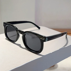 Detail of classic black round frame sunglasses featuring silver rivet studs on a white podium