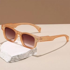 Détail de lunettes de soleil carrées orange mat avec accents dorés sur pierre blanche