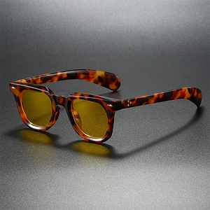 Retro tortoise shell sunglasses with yellow lenses and metallic rivets on dark grey surface