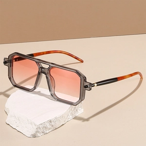 Detail of double-bridge square sunglasses with gradient orange lenses on a stone display