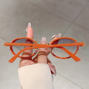 Détail de lunettes de soleil ovales orange avec charnières dorées et verres teintés violets