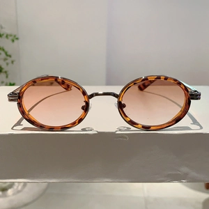 Détail de lunettes de soleil ovales en écaille avec verres roses sur socle blanc