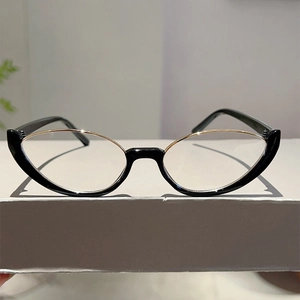 Dettaglio di occhiali cat-eye con montatura nera e oro su un supporto bianco