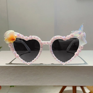 Detail einer herzförmigen Sonnenbrille mit rosa Perlen, Muschel und Meerjungfrauenflosse