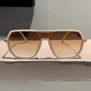 Detail view of white aviator sunglasses with brown gradient lenses on a pedestal