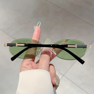 Close-up of rimless oval sunglasses with green tinted lenses and gold metal accents