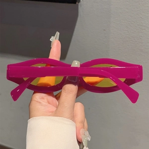 Detail of wavy rose red sunglasses frame with transparent yellow lenses held in hand