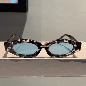 Detail of oval tortoiseshell sunglasses with light blue lenses on a white display stand
