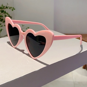 Detail view of heart-shaped sunglasses with pink glossy frames and dark lenses