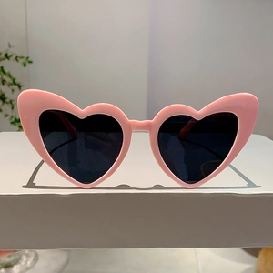 Detail of pink heart-shaped sunglasses with dark lenses on a white display stand