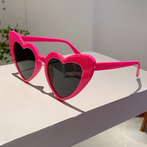 Detail view of heart-shaped hot pink sunglasses with dark grey lenses and resin frame
