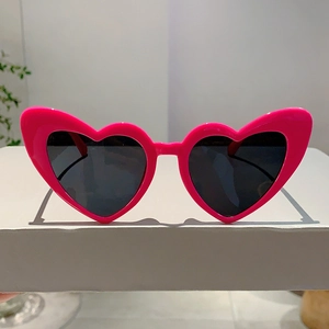 Detail shot of bright pink heart-shaped sunglasses frame with dark gray lenses