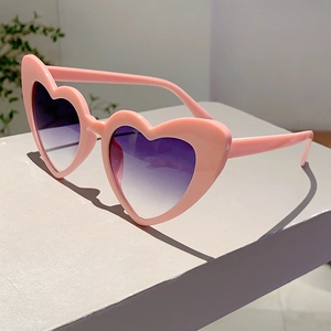 Side view of heart-shaped pink sunglasses with purple gradient lenses on a desk
