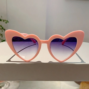 Detail of pink heart-shaped sunglasses with purple gradient lenses on a white display stand