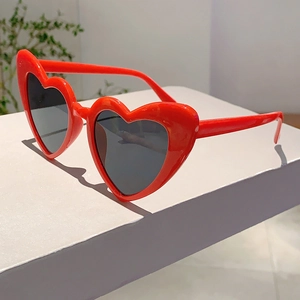 Close-up of bright red heart-shaped sunglasses with dark grey lenses on white display