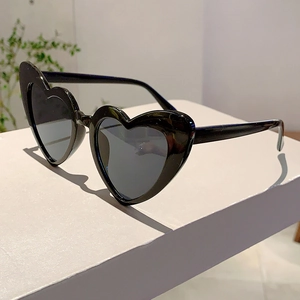 Close-up of heart-shaped sunglasses with thick black frames and dark lenses on a white stand
