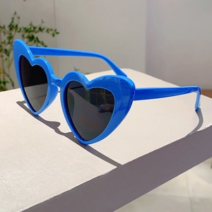 Detail view of bright blue heart-shaped sunglasses with dark lenses on a grey stand