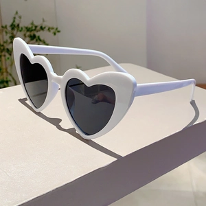 Macro side view of white heart-shaped sunglasses with dark lenses on a grey pedestal