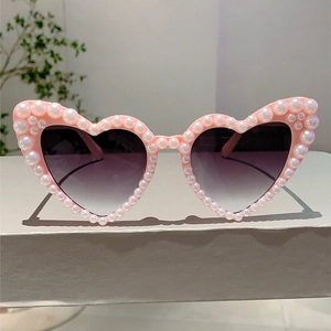 Detail of pink heart-shaped sunglasses featuring white faux pearls and gradient purple lenses