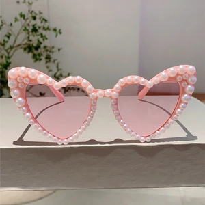 Detail of pink heart-shaped sunglasses featuring double rows of white pearls and pink lenses