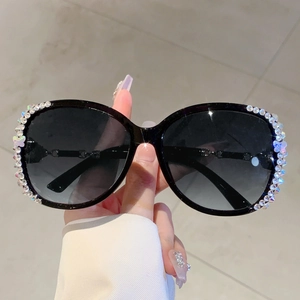 Detail einer übergroßen schwarzen Sonnenbrille mit bunten Strasssteinen und Schmetterling