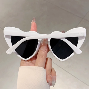 Detail of white heart-shaped sunglasses with wavy frames and dark lenses held in hand