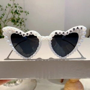 Close-up of white heart-shaped sunglasses with faux pearl trim and Happy Birthday text