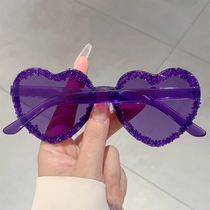 Detail of dark purple heart-shaped sunglasses featuring shimmering glitter-coated edges