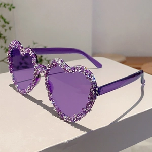 Close-up of purple heart-shaped sunglasses with crystal rhinestones on minimalist desk