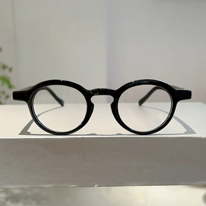Detailed front view of round black retro eyeglasses on a gray minimalist display stand