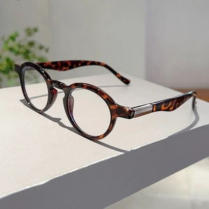 Side view of round tortoiseshell glasses with silver metal accents on a grey stand