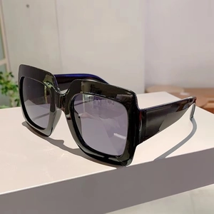 Detail of square oversized black sunglasses with wide temples on a minimalist display
