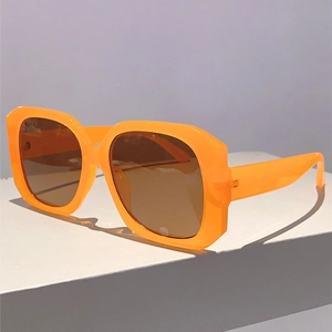 Detail view of square orange frame sunglasses with dark brown lenses on a white block