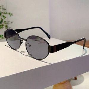 Close-up of black oval sunglasses with polished metal frame and tinted lenses on a white stand