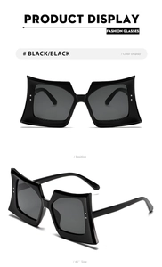Detail of oversized geometric butterfly sunglasses with glossy black frames and dark lenses