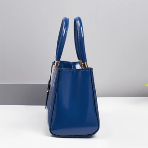 Detail of navy blue patent leather handbag with glossy finish and gold metal hardware