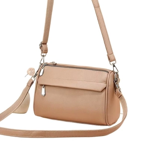 Brown leather crossbody bag with dual zippers, wide strap, and pink pompom keychain detail